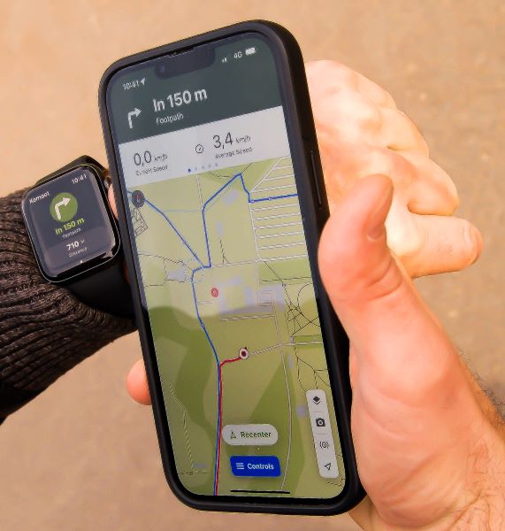 photo d'un smartphone sur lequel une carte avec une fonction de géolocalisation est affichée, l'homme qui tient le téléphone a aussi une smartwatch qui elle affiche la prochaine direction à prendre